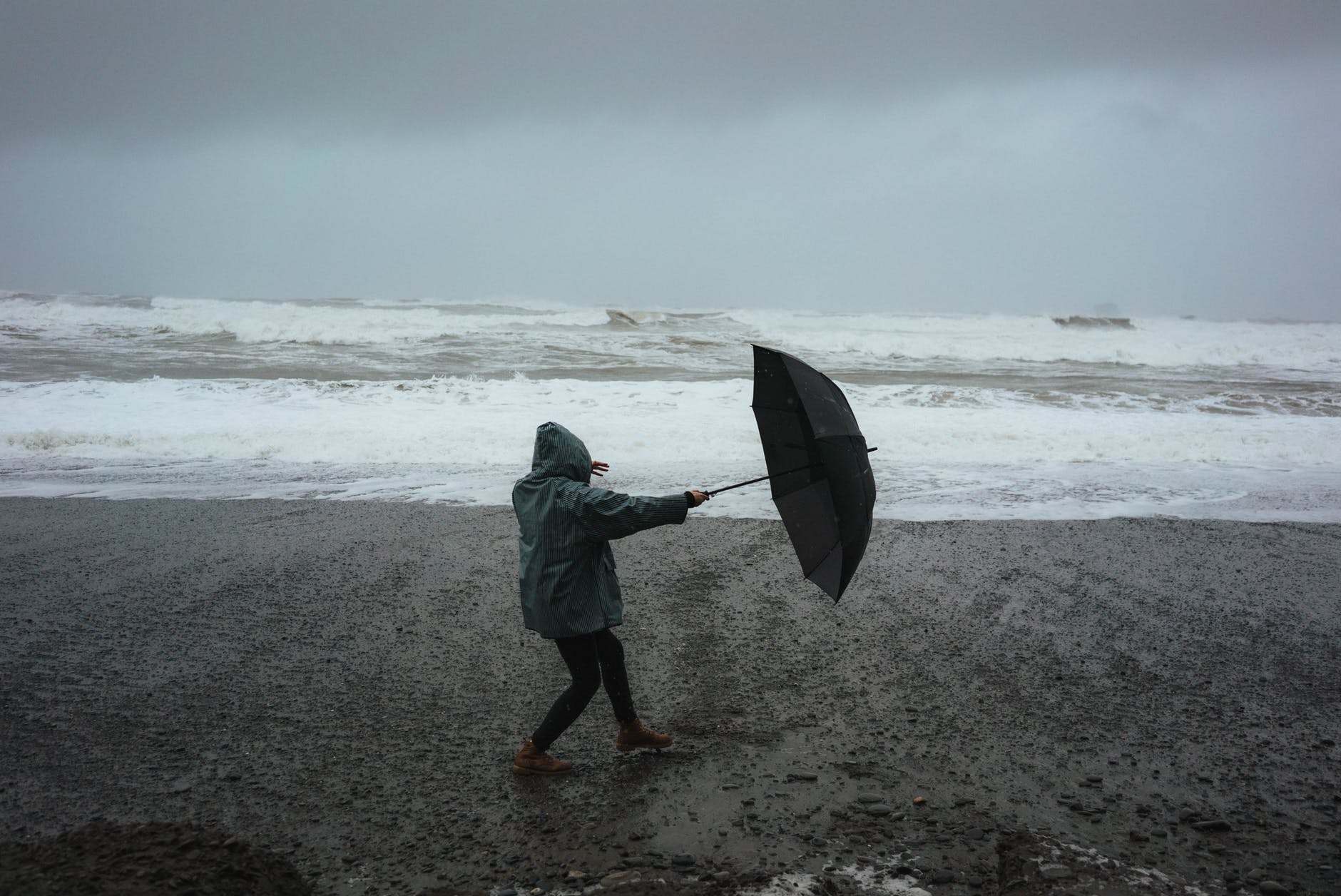 Person with an umbrella on the beach in a storm.