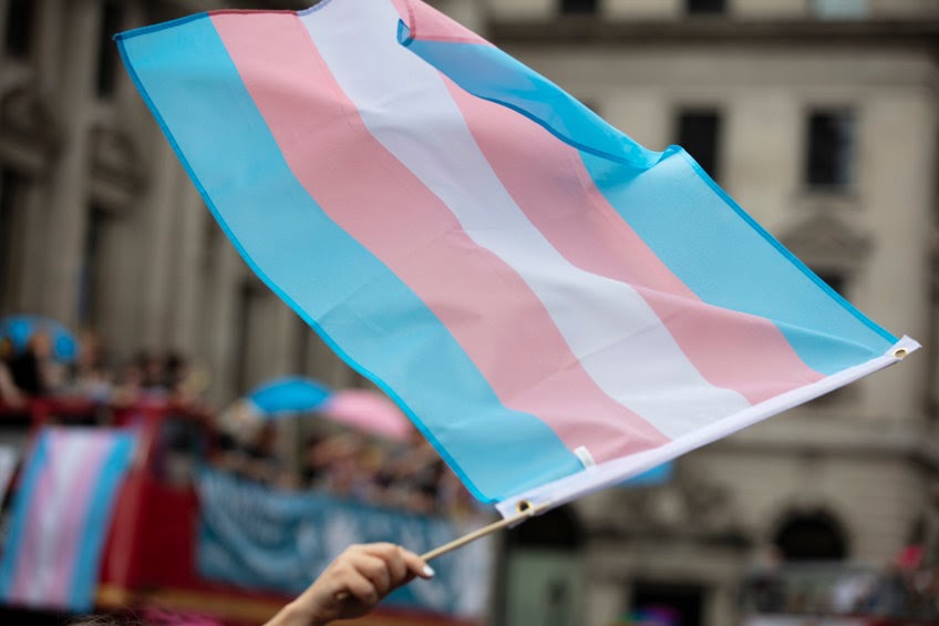 A person waving a transgender flag. It is critical to honor our transgender siblings as co-bearers of the image of God.