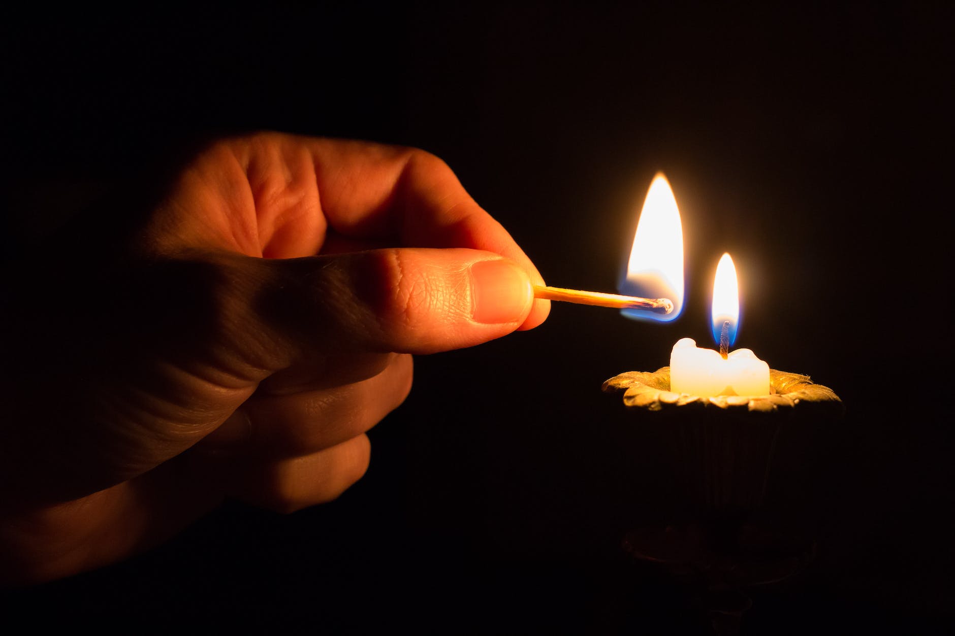 person holding match stick with fire in front of candle with fire. Waiting in the dark.